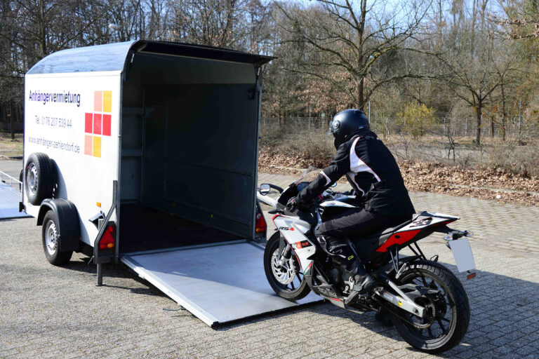 Ein Motorradfahrer fährt sein Motorrad in einen geschlossenen Anhänger.
